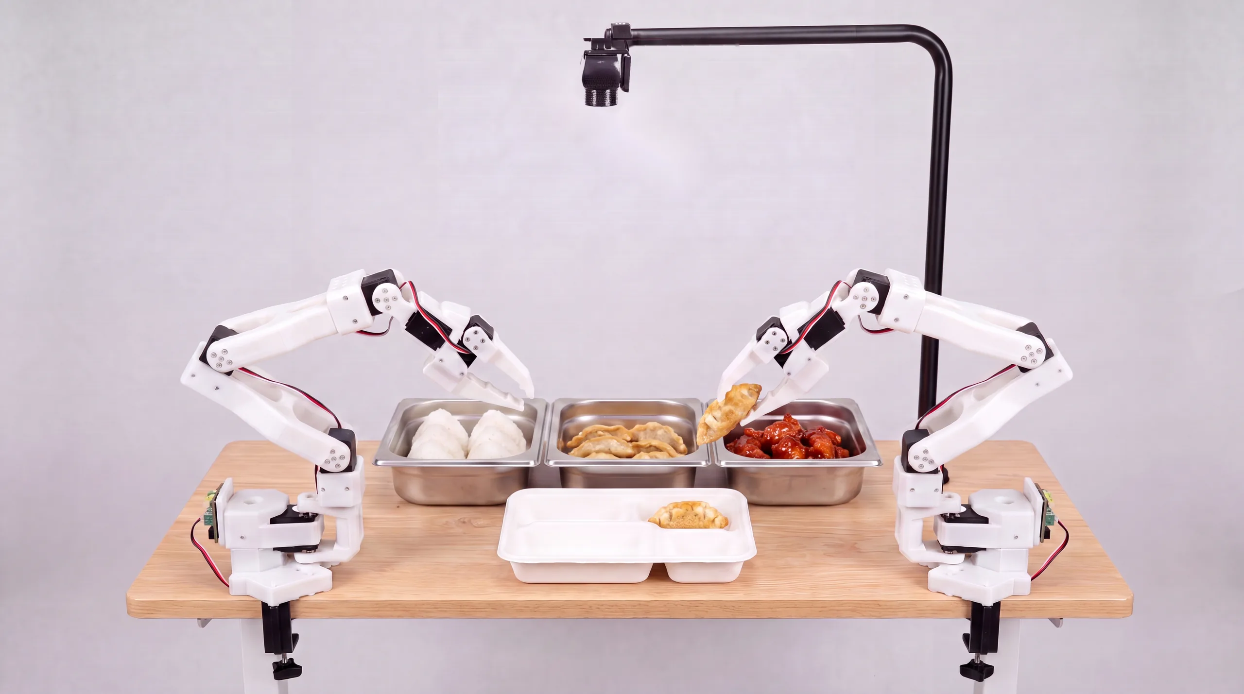Two robot arms portioning food from steel hotel pans into a compartment meal tray